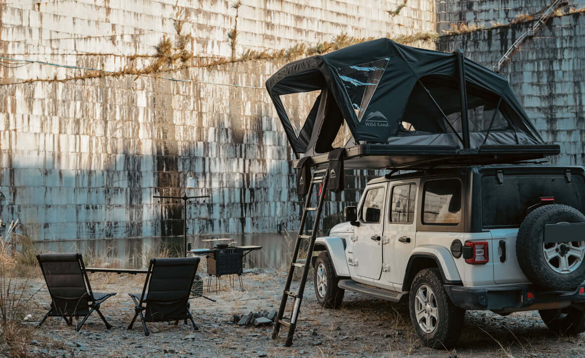 Jeep Wrangler con tenda da tetto Wild Land aperta e campo tra le rocce
