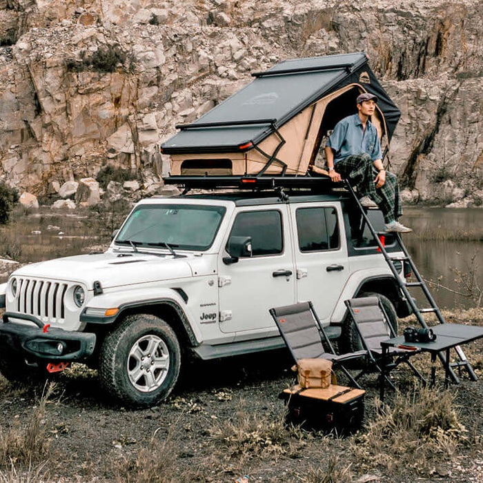 Jeep Wrangler bianca con tenda da tetto Wild Land aperta e campo tra le rocce