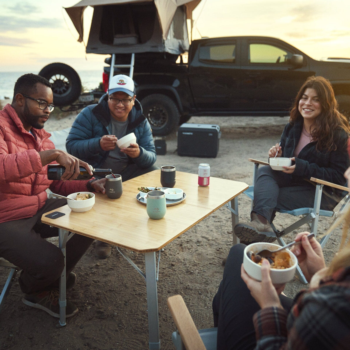 Cena per quattro al Dometic GO Compact Camp Table vicino a un pick-up con tenda da tetto