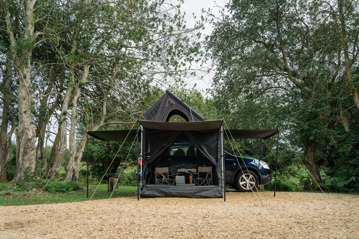 Tendalino laterale Tendbox 2.3m installato su tenda, circondato da alberi e auto nel campeggio.