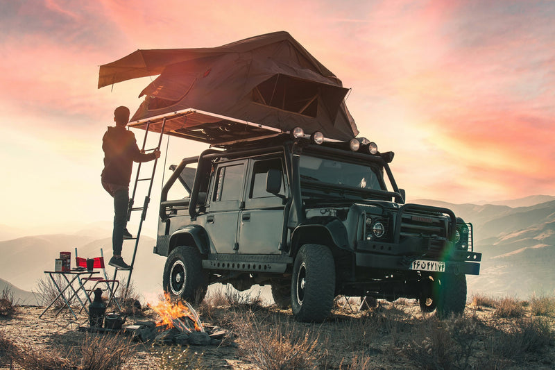 Land Rover Defender con tenda da tetto aperta e campo al tramonto