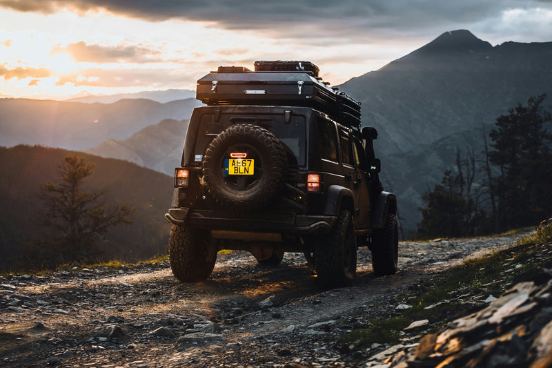 Jeep Wrangler con tenda da tetto rigida su pista di montagna al tramonto