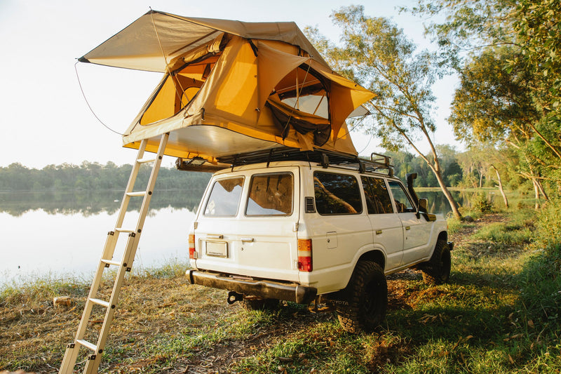 Toyota Land Cruiser con tenda da tetto aperta in riva al lago all'alba