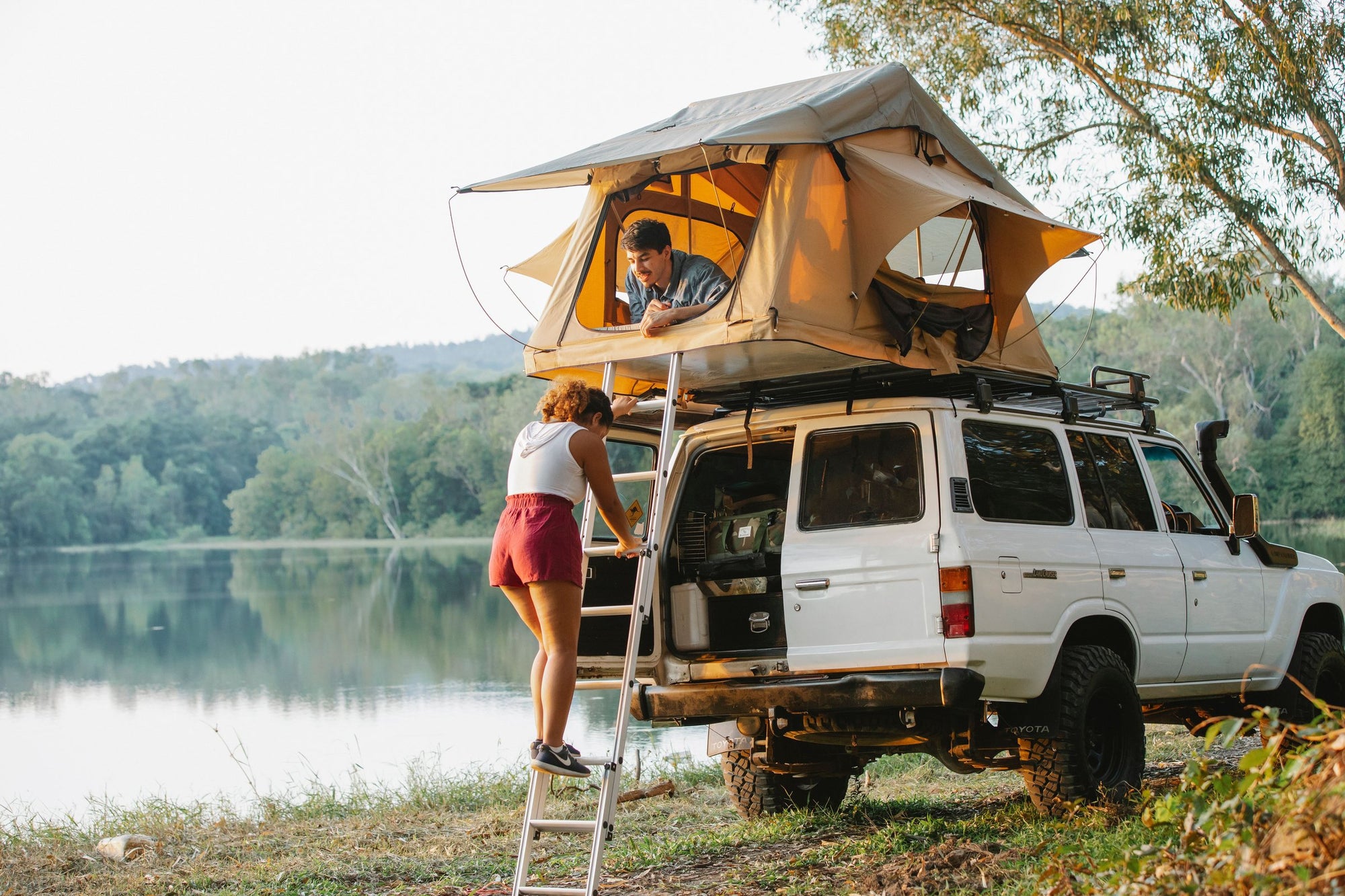 Coppia con tenda da tetto su Toyota Land Cruiser in riva al lago