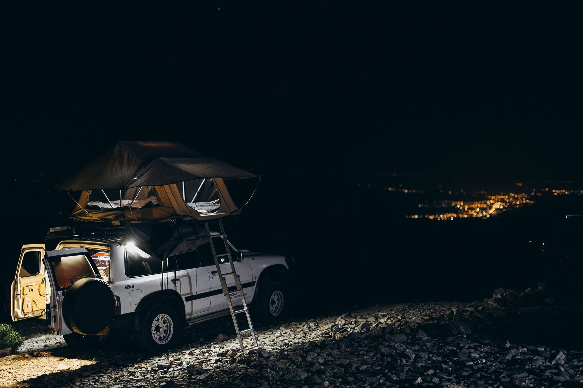 Nissan Patrol con tenda da tetto aperta di notte sopra la valle illuminata