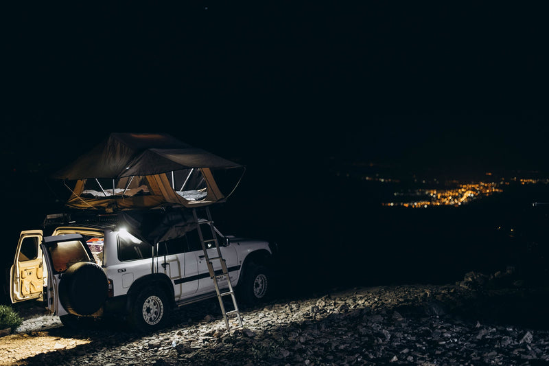 Nissan Patrol con tenda da tetto aperta di notte sopra la valle illuminata