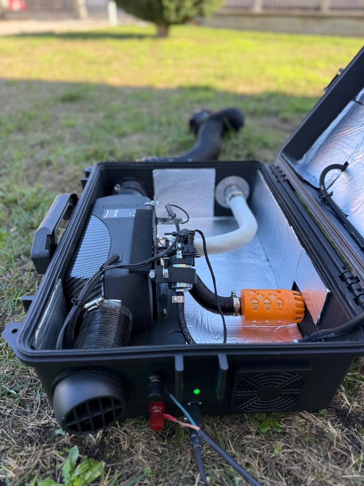 Valigetta ARGOING OverlandHeat aperta su un prato con riscaldatore, condotti, pulsante di accensione e tubo
