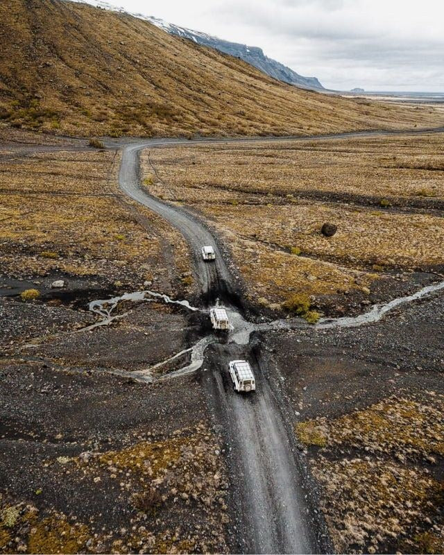 Tre Land Rover Defender attraversano un torrente su una pista islandese vista dall'alto