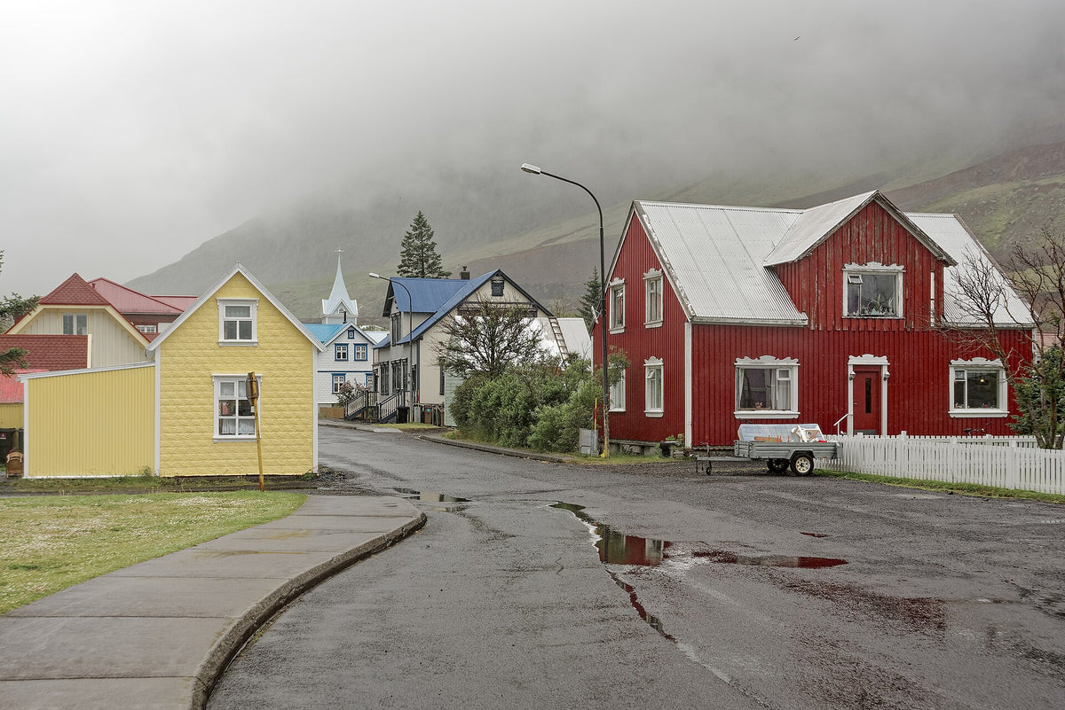 Case colorate in legno lungo una strada di Seyðisfjörður con montagne nella nebbia