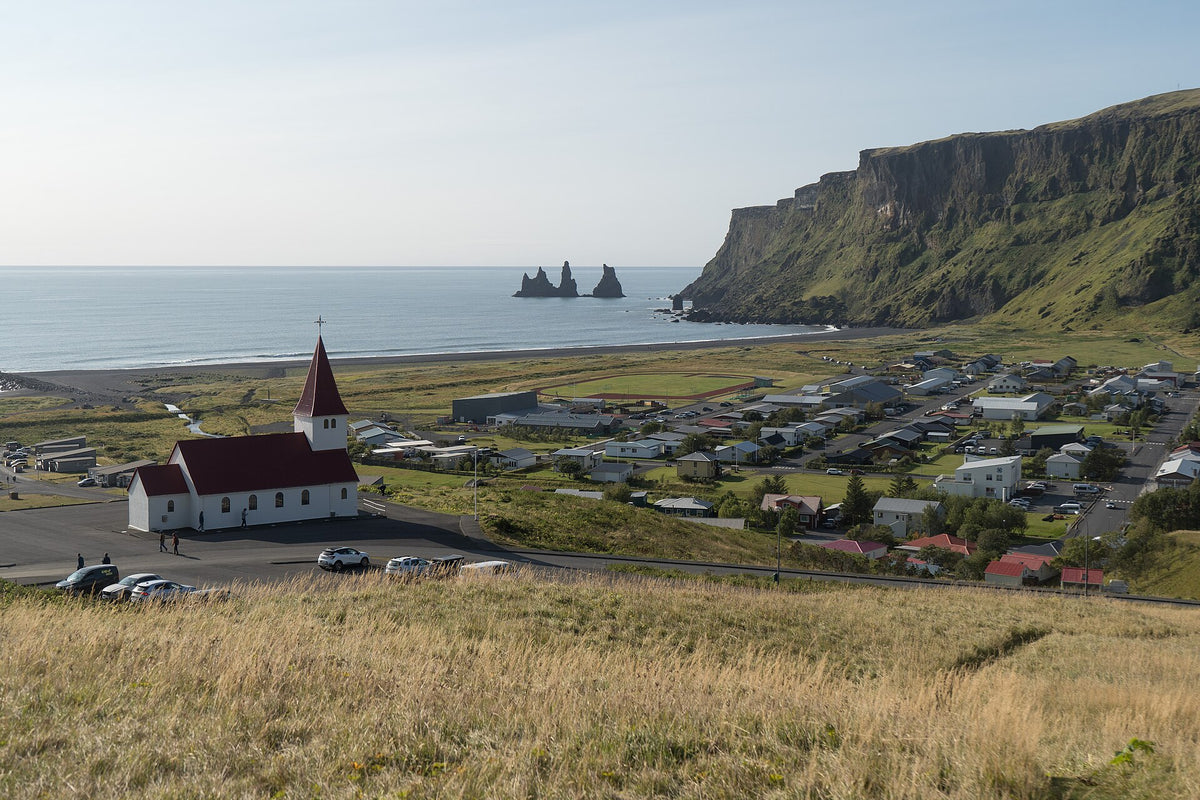 Il paese di Vík í Mýrdal con la chiesa rossa e bianca, le scogliere e i faraglioni Reynisdrangar sul mare